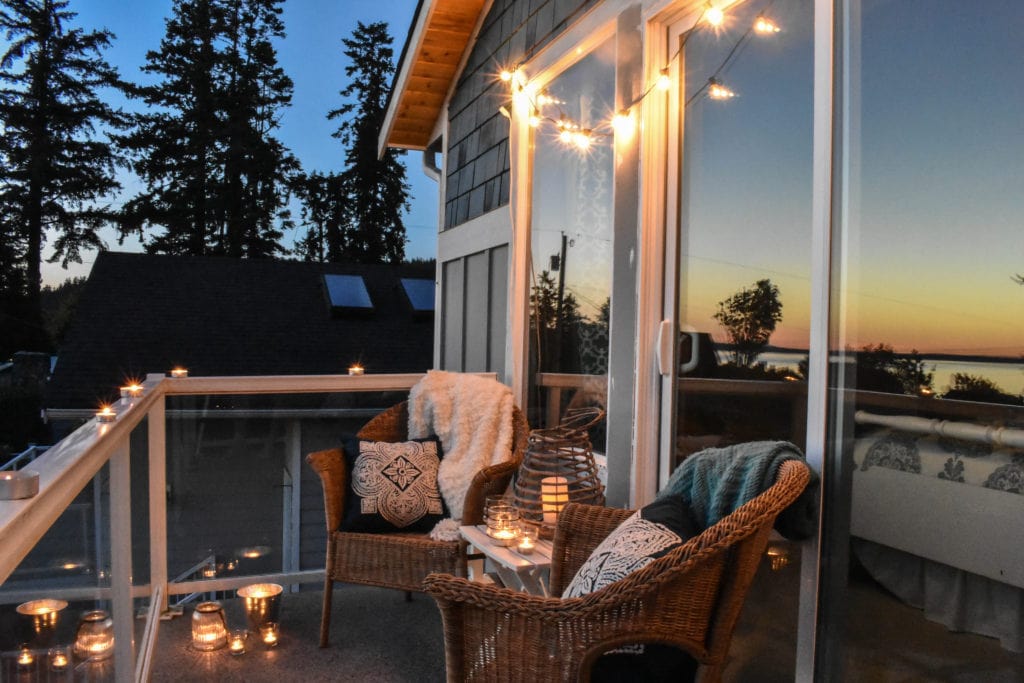 balcony with two chairs and a small table lit by string lights and candle lanterns