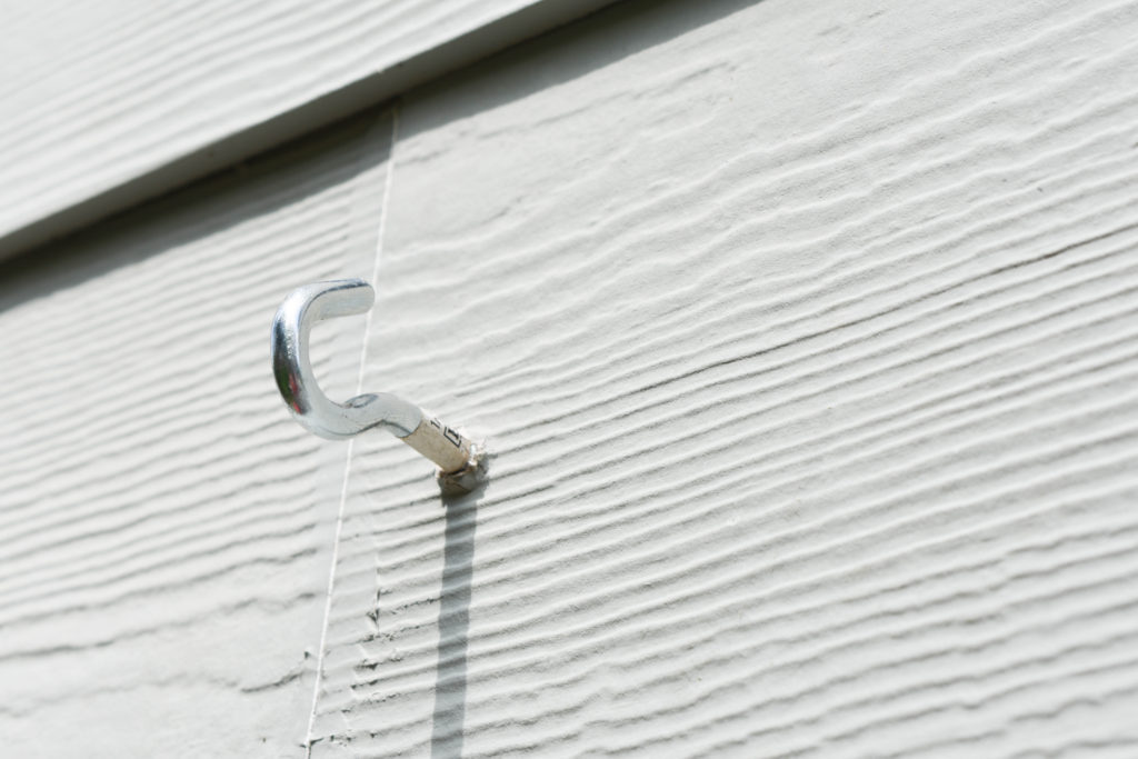 close-up of metal hook installed on the exterior wall of a house to hang string lights over a patio