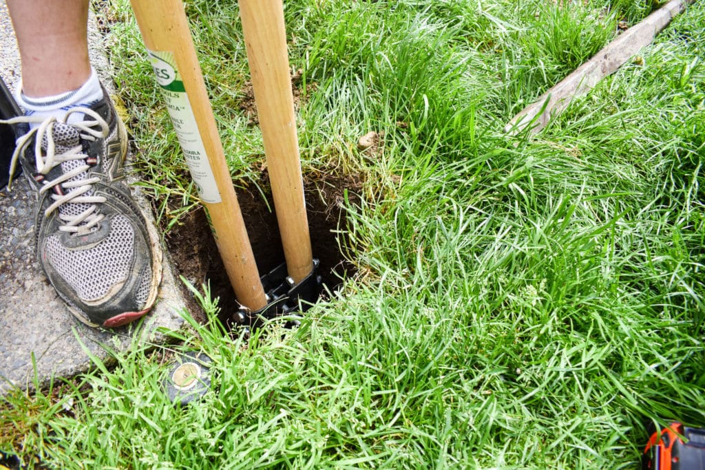 close-up of someone using a post hole digger to dig a hole for an in-ground string light pole to hang patio lights, how to string lights across backyard
