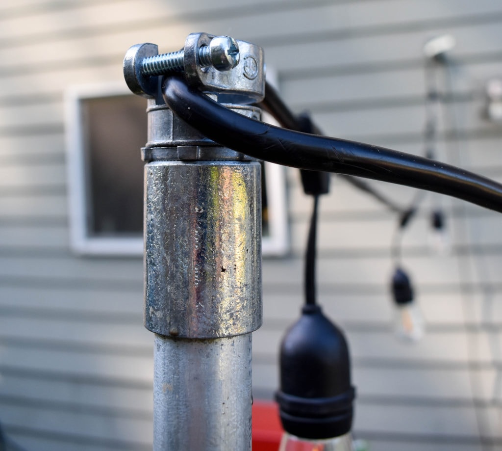 close-up of the tops of a string light pole, with black cafe lights hanging over a patio