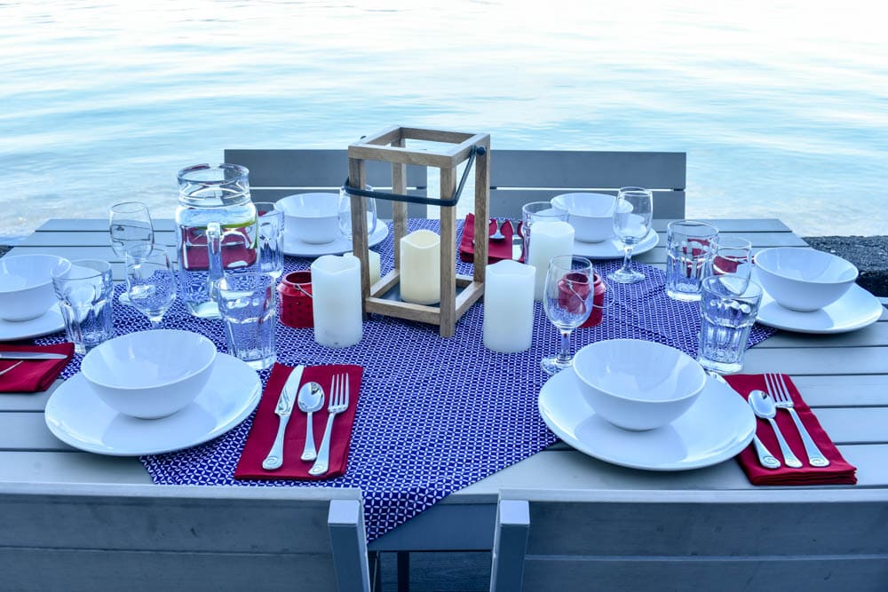 outdoor dining table set for an independence day party with red white and blue decorations and candles in front of water