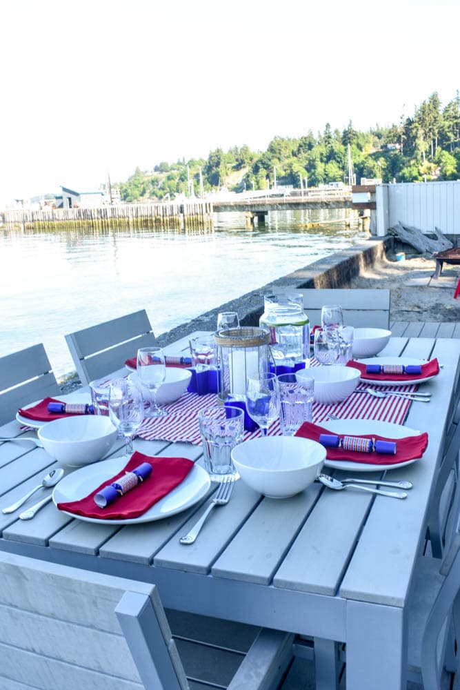 Patriotic table decorated for a 4th of July party with red and white striped fabric, red cloth napkins, party poppers, and candle lanterns