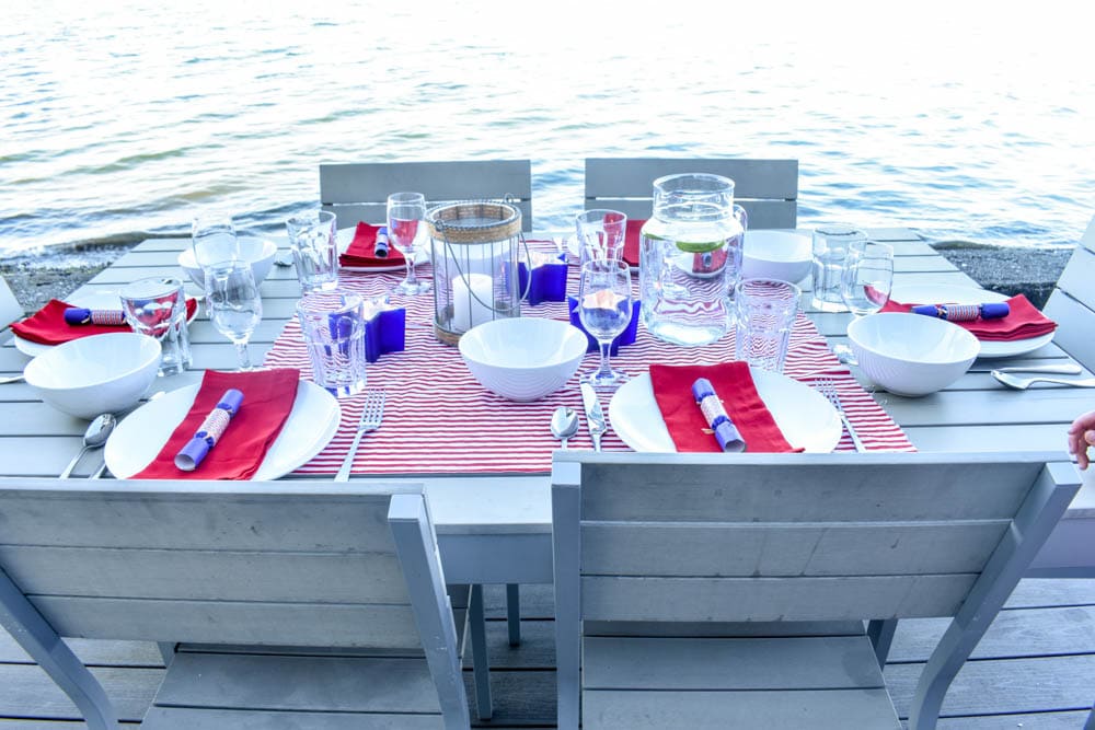 4th of July table set with red and white striped fabric and blue party poppers, with candle lanterns in front of Puget Sound