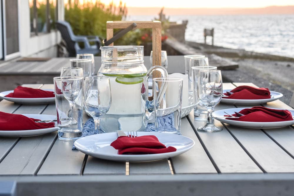 Table set for a 4th of July dinner with navy blue and white table runner and red cloth napkins, and sunset in background