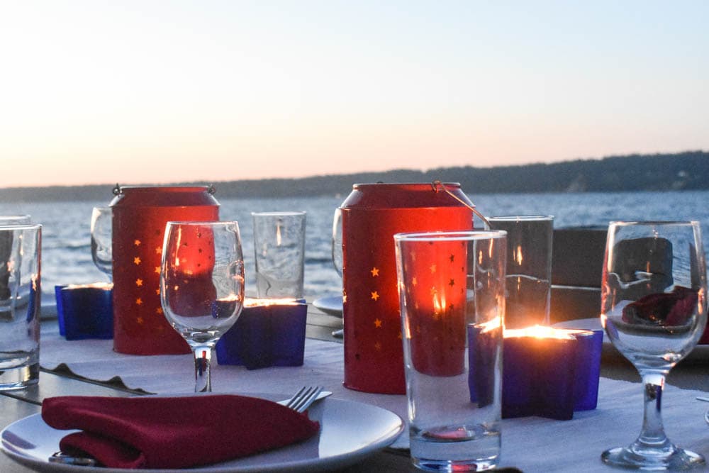 Independence Day table set with glowing red and white candle lanterns in front of Puget Sound