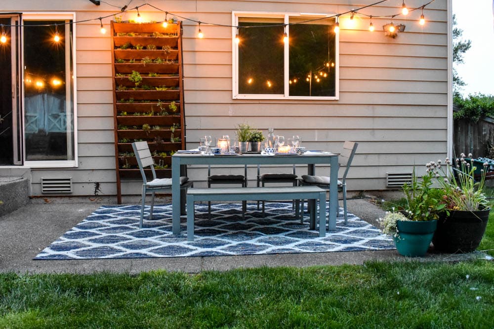 outdoor dining area on a patio with easy diy string light poles and instructions on how to hang string lights across the backyard