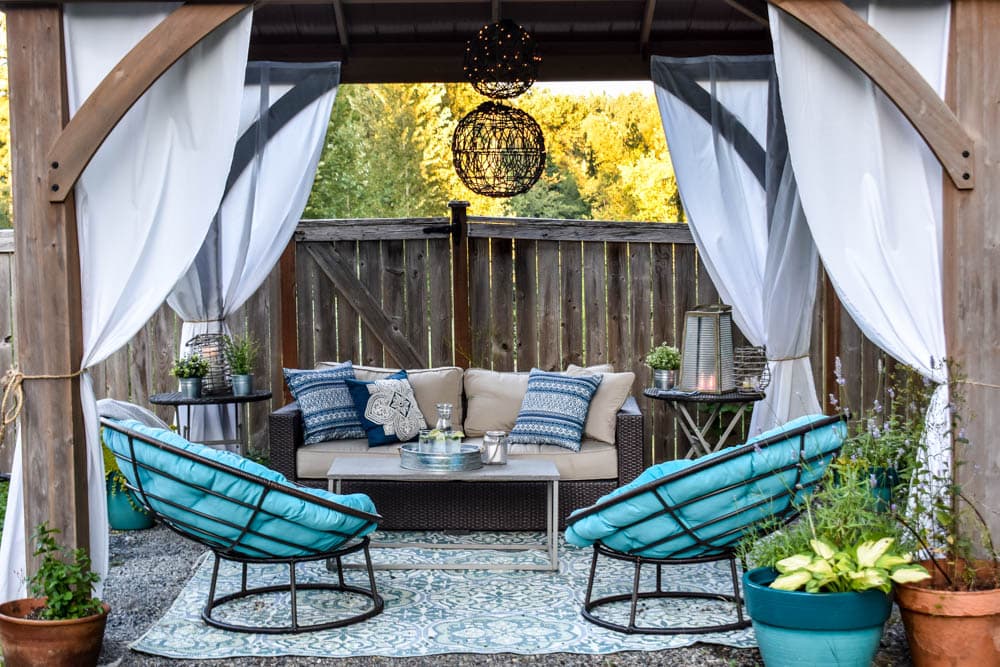 This covered outdoor living room on a budget is the perfect backyard Summer spot to relax! It's got a fireplace to roast marshmallows, cozy modern furniture, and an outdoor rug.