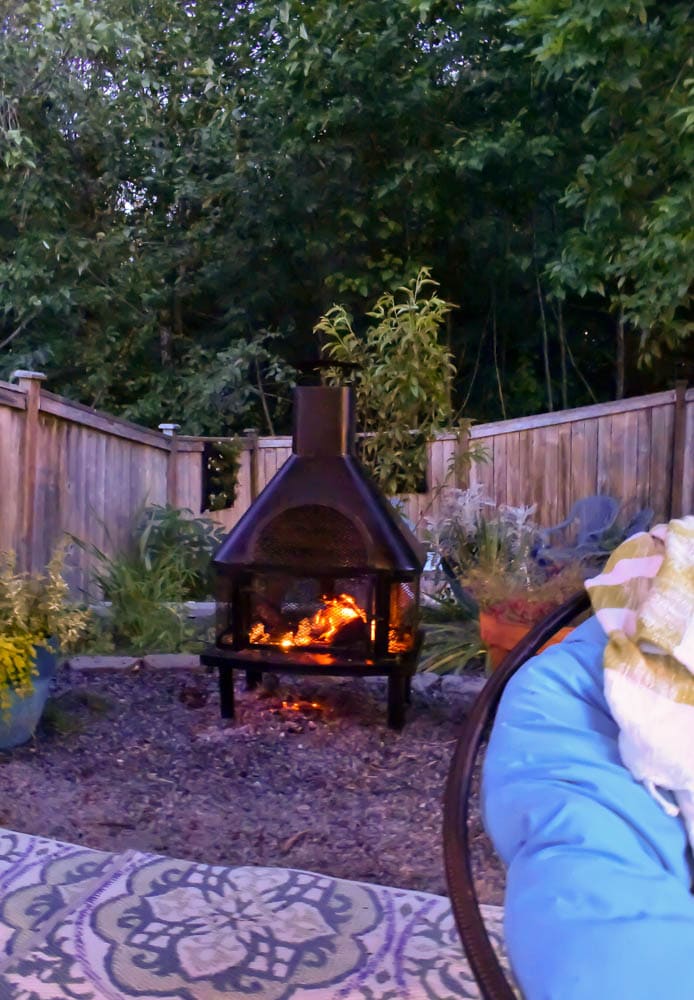 This covered outdoor living room on a budget is the perfect backyard Summer spot to relax! It's got a fireplace to roast marshmallows, cozy modern furniture, and an outdoor rug.