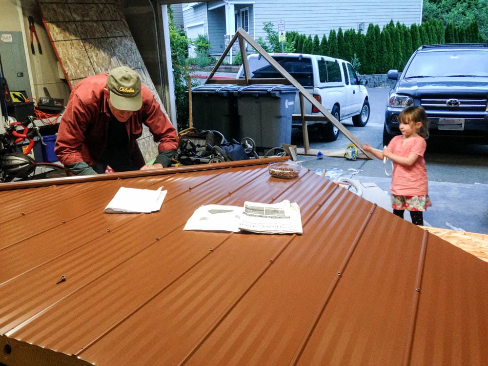 férfi és kislány a Costco Gazebo by Yardistry Structures tetőszekcióinak összeszerelése a garázsban.