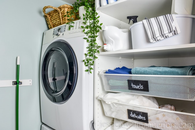 This small laundry room makeover on a budget makes the most of every square inch! It includes a stackable washer and dryer, sorting space, laundry basket storage, an ironing board, and space for detergent and cleaning supplies!