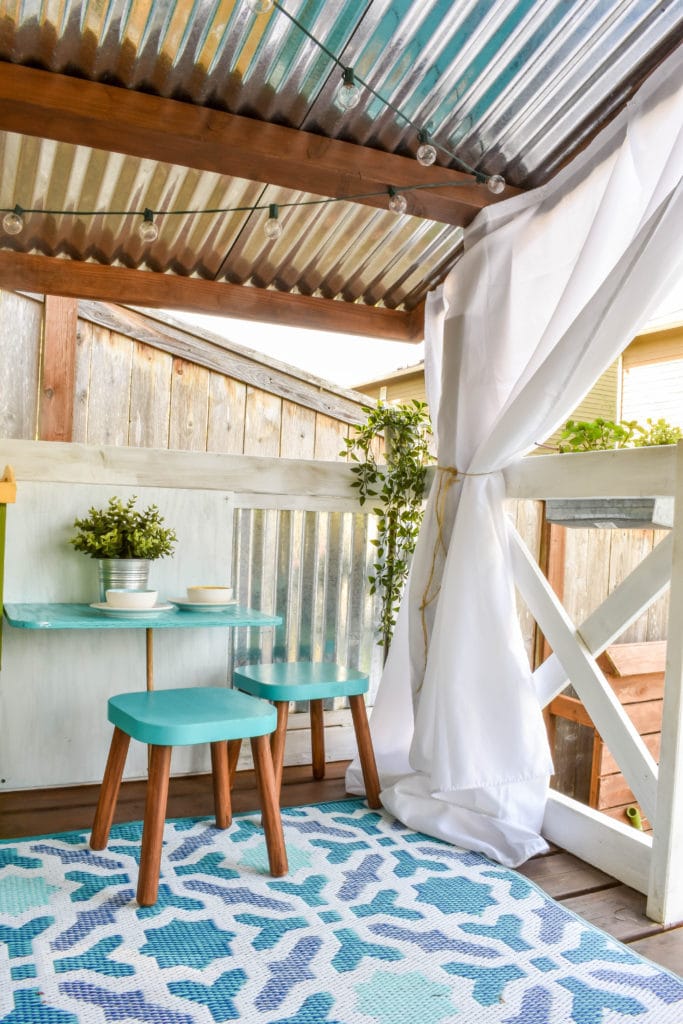 image of interior of playhouse with curtains, string lights, and mini table and stools