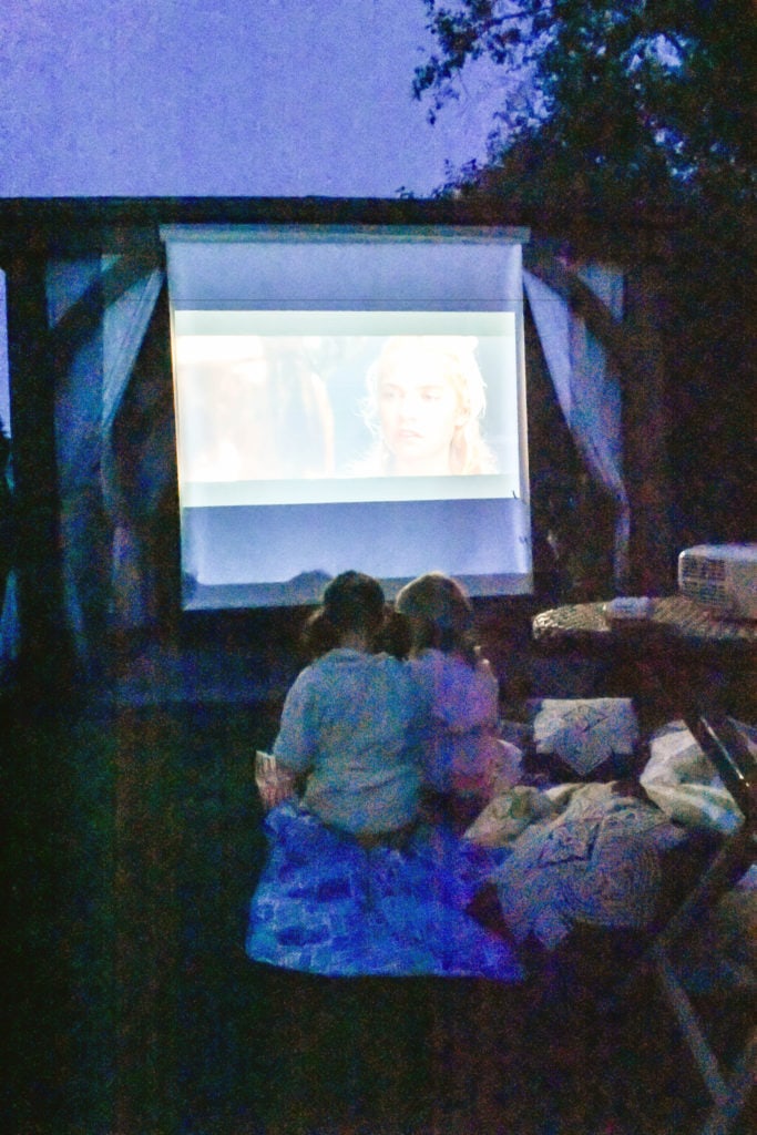 Cine en el patio trasero montado usando Costco Gazebo por Yardistry. Dos niñas viendo la película en primer plano frente a la pérgola de Costco