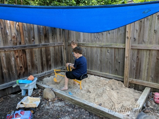 two small boys playing in sandbox covered in a blue shade sail