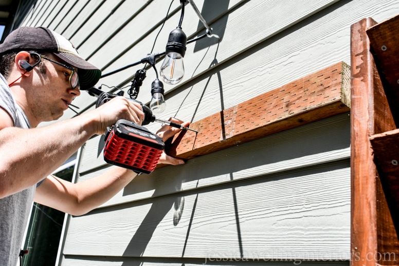 image of man attaching 2x4 mount to the side of house with screw gun