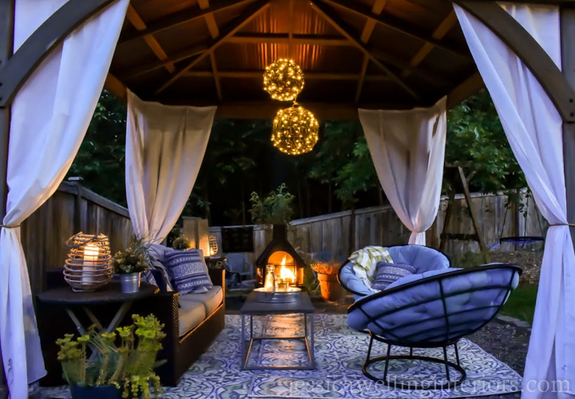 outdoor living room in a gazebo with outdoor chandelier, outdoor fireplace, and candle lanterns