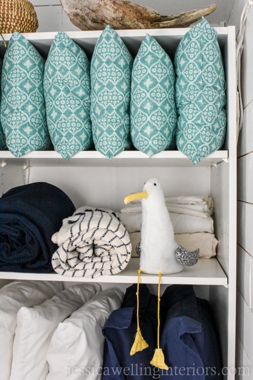 IKEA PAX wardrobe shelf hack used as an open linen closet in a beach house bunk room with a stuffed seagull