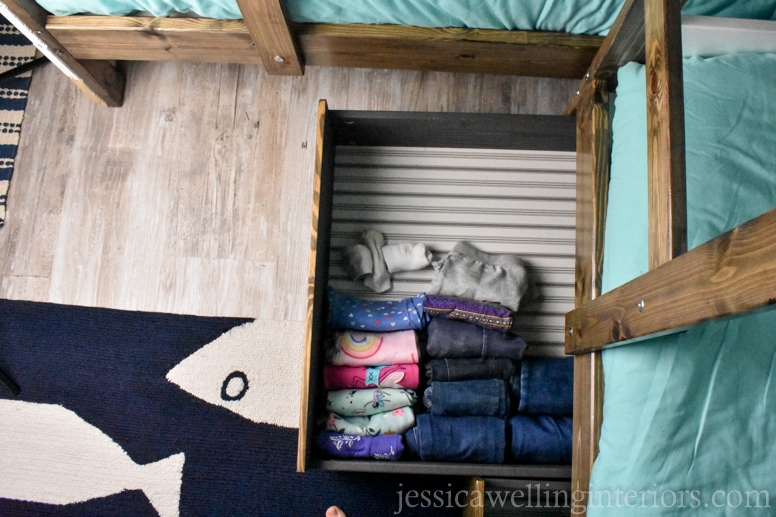 IKEA bunk bed room with HEMNES under-bed storage drawer hack. Drawer is pulled out with folded clothing inside