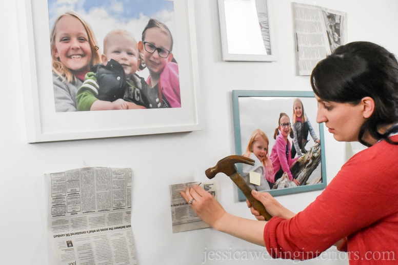 woman using a hammer to mount framed photos on gallery wall in beach house bunk room
