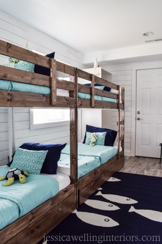 4 bunk beds in a beach themed bunk room with a navy fish rug and stuffed sea creatures on the beds