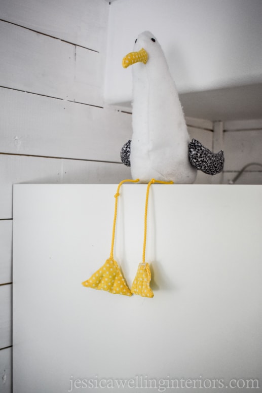 homemade stuffed seagull sitting on top of a bookshelf in a beach house bunk room