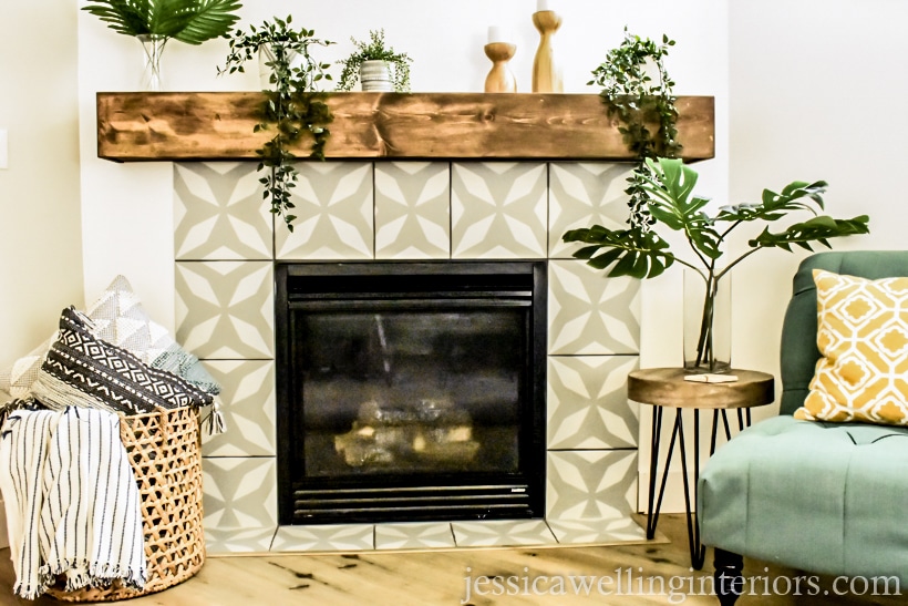 completed painted faux cement tile fireplace makeover with grey and white stenciled tile, new wood mantel, a basket with blankets and throw pillows, and a chair