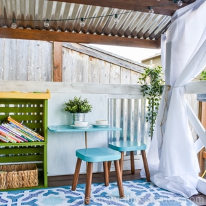 interior of playhouse with string lights, outdoor rug, table and chairs, and a bookcase