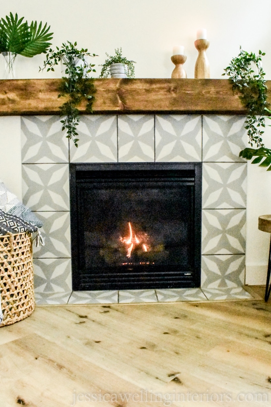 after photo of fireplace makeover- gas fireplace with faux painted cement tile in a grey and white morroccan pattern with a wood box mantel and indoor plants