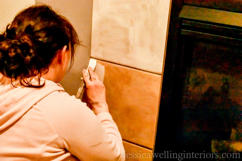 woman applying BIN primer to tile fireplace surround with a paintbrush before painting and stenciling tiles