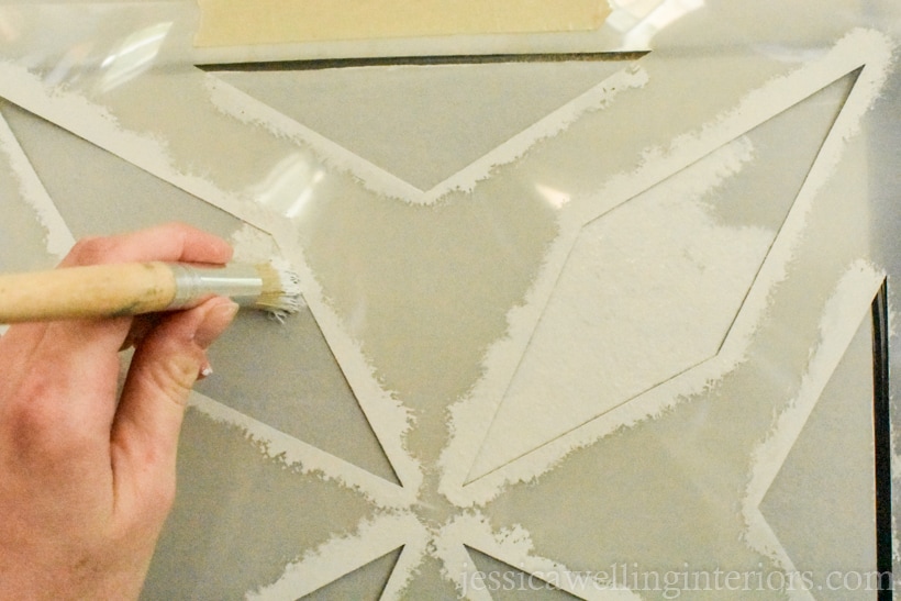 hand holding stencil paintbrush, dabbing paint onto tile to create a faux cement tile pattern