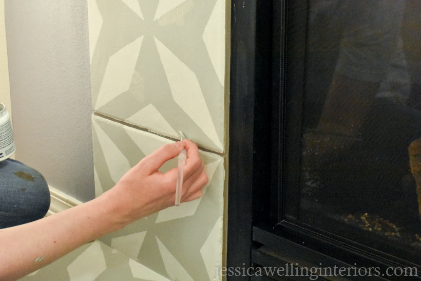hand using a small angled artist's brush to touch up stencil pattern after removing the stencil to create a faux cement tile look around the fireplace
