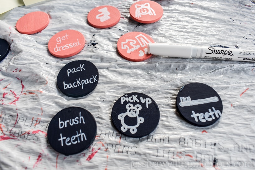painted wood coins- some navy blue and some coral pink, with words and pictures written with a white sharpie paint pen for kids morning routine charts
