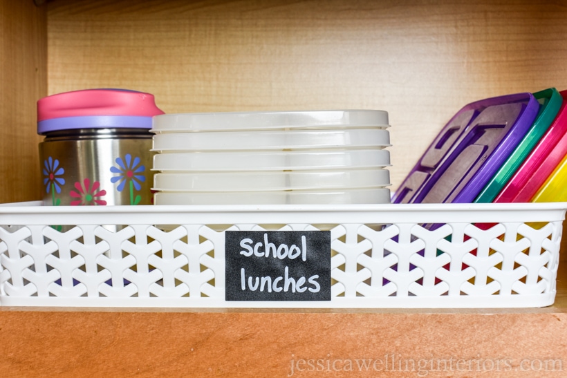 kitchen cupboard with basket labeled "school lunches" and thermos and stack of bento containers with lids