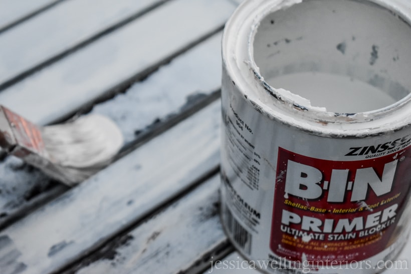 open can of Zinsser BIN primer sitting on rusty patio table, with paintbrush applying primer in the background