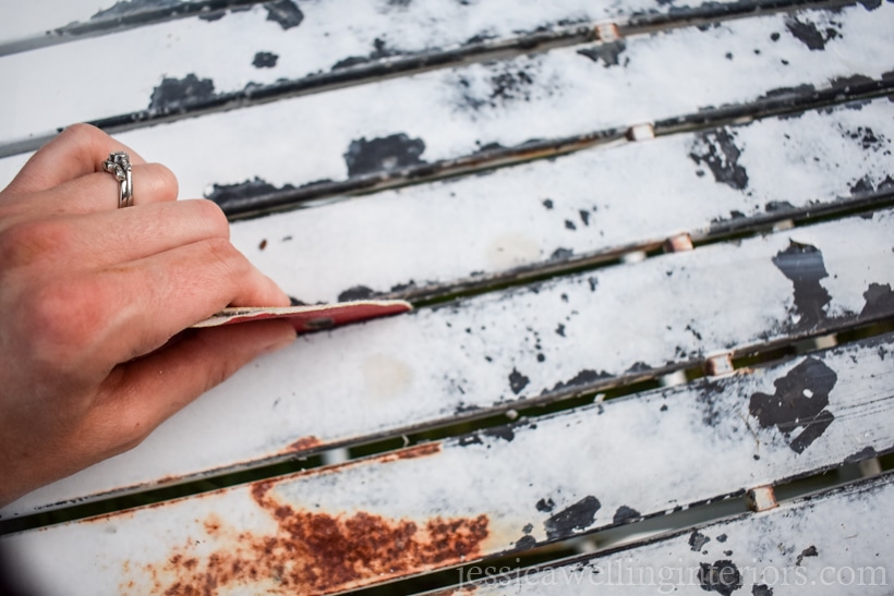 close-up of hand sanding peeling paint off of old rusty metal patio table