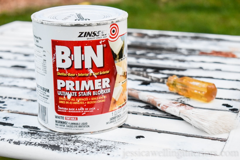 can of Zinsser BIN primer, paintbrush, and flatblade screwdriver sitting on old rusty patio table