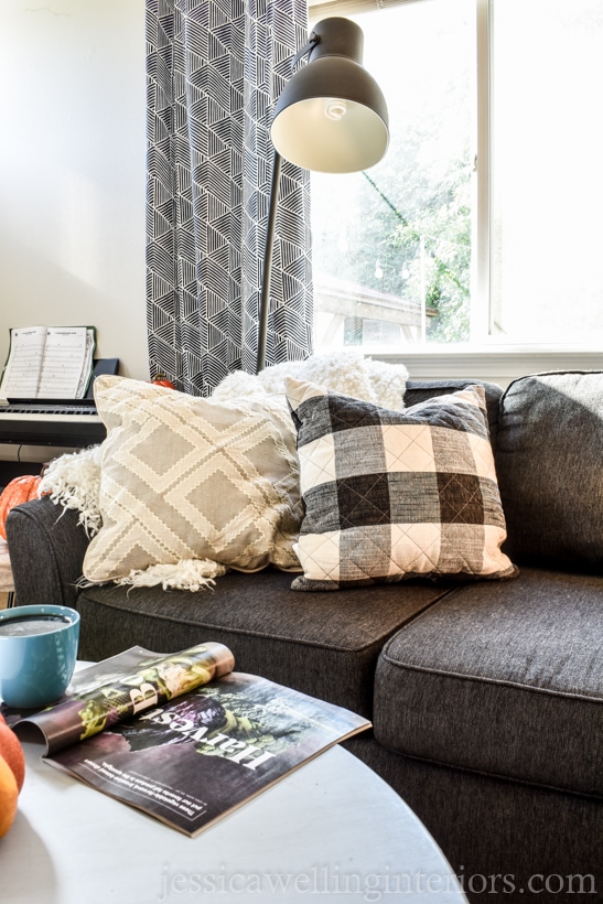 Neutral fall living room decor with charcoal sofa, fluffy white throw blanket, white pillow, and black and white buffalo plaid throw pillow