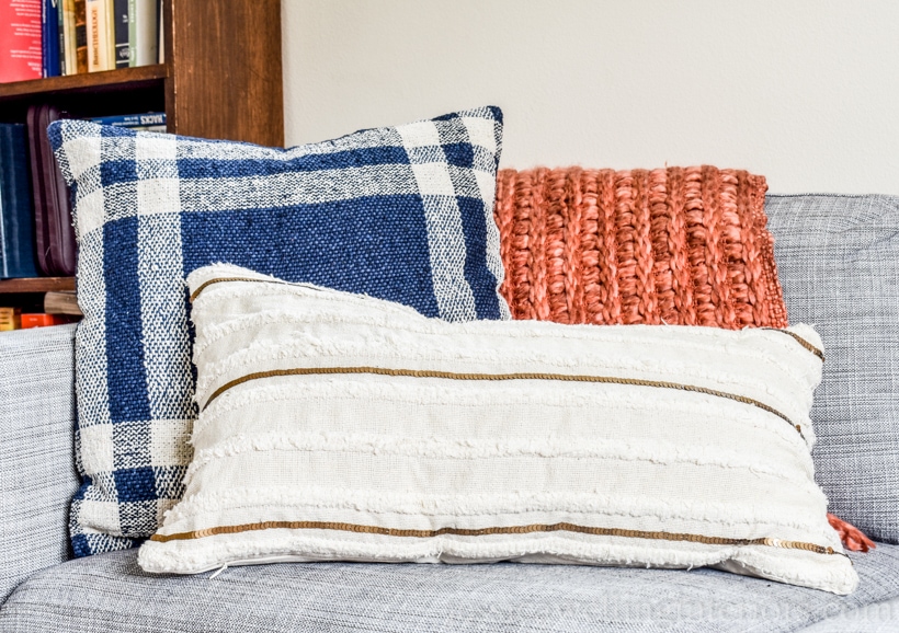 Fall living room decor with navy and white plaid throw pillow, burnt orange chunky throw blanket, and white boho lumbar pillow