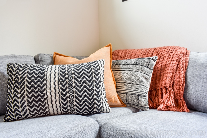 living room sofa decorated for Fall with burnt orange chunky throw blankets, tribal black and white patterned throw pillows, and a yellow pillow