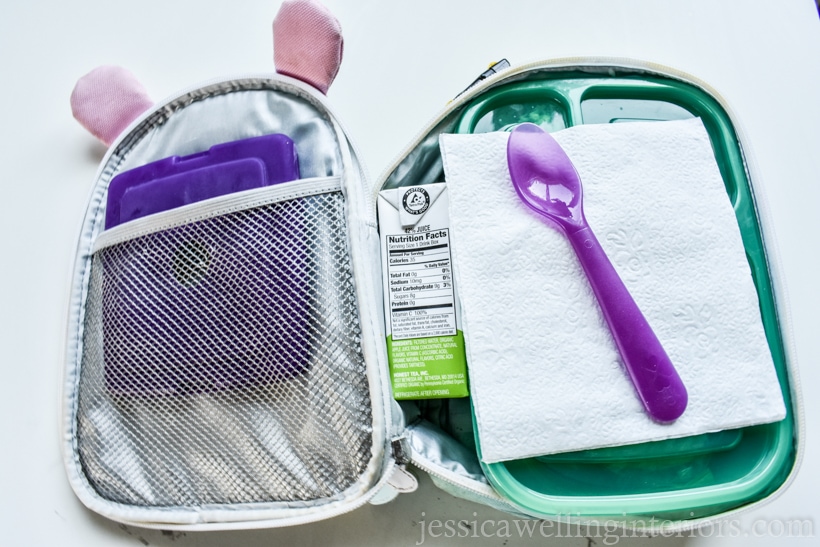 open childn's lunch box packed with an ice pack, a bento-style container, plastic spoon, and juice box