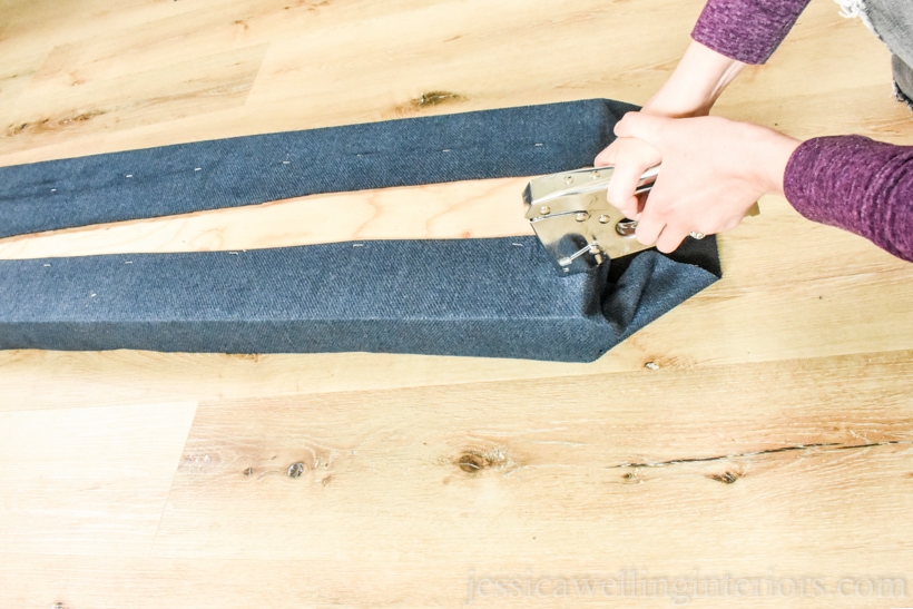 hand using staple gun to wrap and staple the fabric on the end of upholstered bench seat cushion for window seat