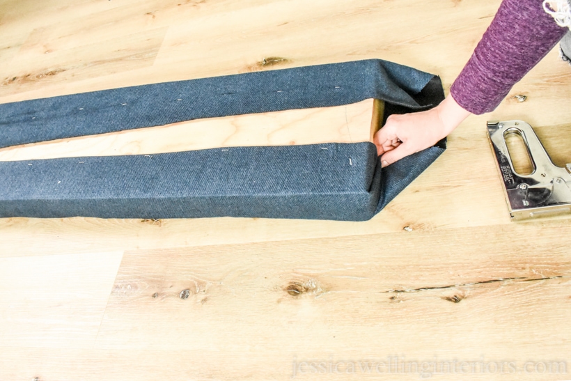 hand wrapping fabric before using a staple gun to staple it to the plywood backing of the window seat cushion