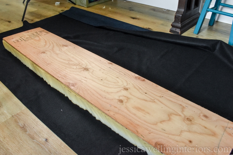 navy upholstery fabric laid out on floor, with cut foam and plywood on top of it to make an upholstered bench cushion