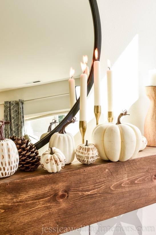 wood mantel with white painted pumpkins, gold candlesticks, and a pinecone