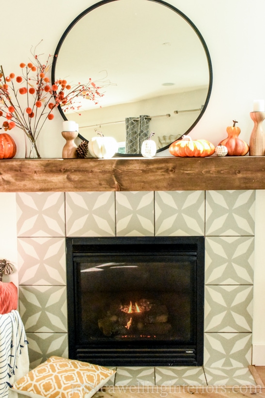 modern fireplace with round black-framed mirror, Fall decor stems in a vase, pumpkins, and a yellow throw pillow on the floor