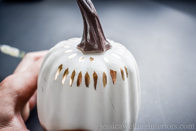 hand holding a white painted pumpkin with gold leaf painted lines