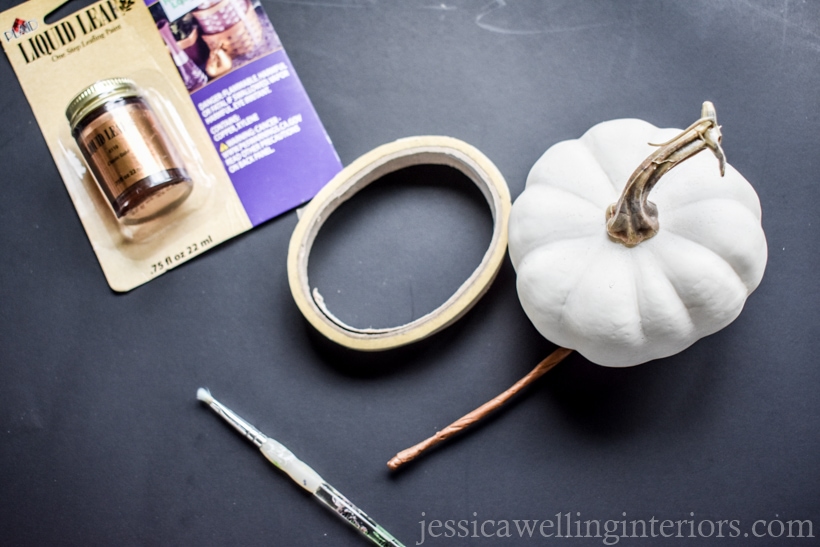 supplies to paint pumpkins for Fall decor- white faux pumpkin, gold leaf paint, small paintbrush, and masking tape against a black background