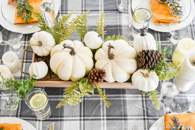 Thanksgiving table setting with grey and white plaid tablecloth, white pumpkin centerpiece, and mustard yellow cloth napkins
