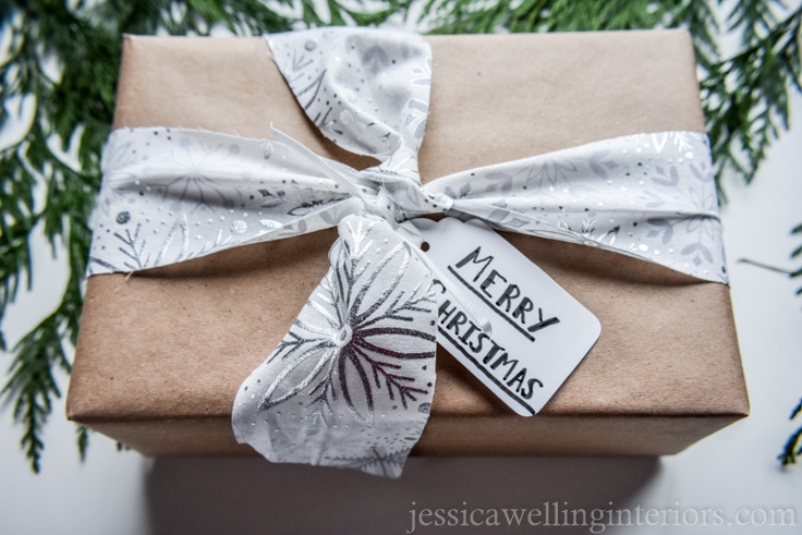 Christmas gift wrapped in brown paper and tied with white and silver fabric ribbon with snowflake pattern