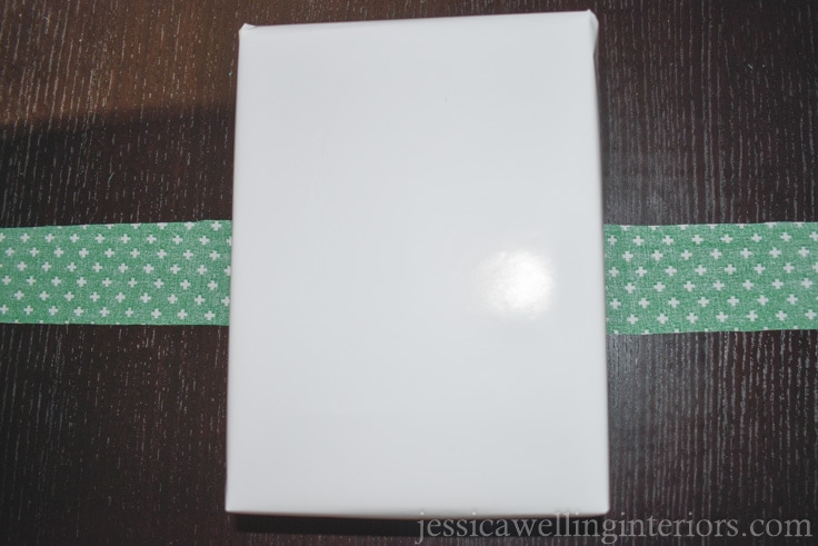 Christmas gift wrapped in solid white wrapping paper, laying on top of strip of green fabric