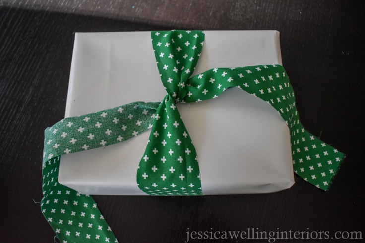 green fabric "ribbon" being tied in a knot on top of white-paper wrapped Christmas gift